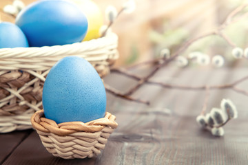 Easter composition - several colored eggs in a basket and on a dark wooden table with willow twigs
