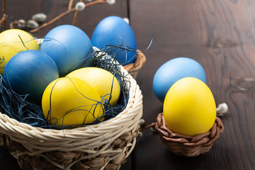 Easter composition - several colored eggs in a basket and on a dark wooden table with willow twigs, place for text, copy space