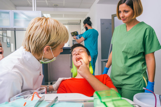 Female dentist with the help of her dentist technician examines the mouth and teeth of a teenage boy patient.