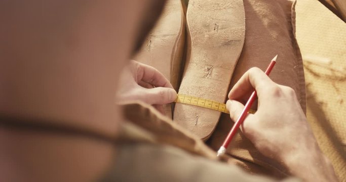 Traditional bespoke shoemaker measuring marking leather insole on wooden shoe last with tape measure pencil over the shoulder