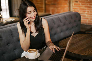 Business woman working on a laptop, using phone and drinking coffee in a cafe.