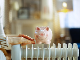 Closeup on woman near radiator with piggy bank warming hands