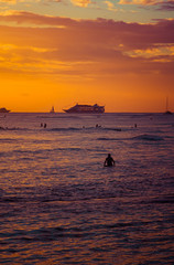 Surfer relaxing in the Pacific Ocean during sunset with a cruise ship on the horizon in Hawaii.