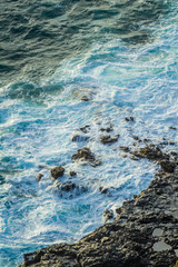 Sea foam from rough ocean surf against the rocky shoreline of Hawaii.