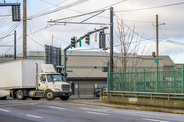 Big rig day cab semi truck with roof spoiler transporting goods in dry van semi trailer turning on...
