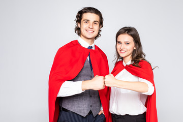 Young couple of superheroes in costumes standing with hands to hands and looking at camera isolated on white background