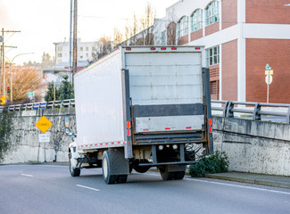 Big rig semi truck transporting cargo in box trailer driving on the city street road running down the hill