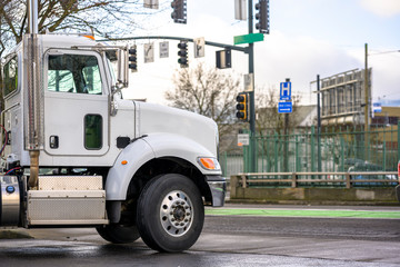 Day Cab Powerful Big Rig Semi Truck Standing on the Parking Lot on the City Street Intersection with Traffic Lights