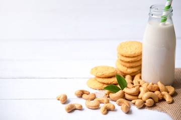 Vegan milk from cashews  in  bottles and cashew nut cookie on  white wooden surface, Cashew nuts is used in most indian sweets with copy space.