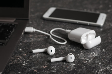 A case of wireless headphones connected to a laptop and a smartphone on a stone background.