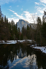 Half Dome and surrounding woods reflected in Merced River in Yosemite National Park, California under winter cloudscape.