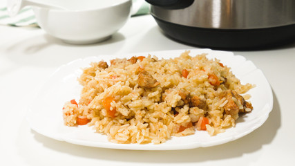 Rice with meat and vegetables (Rice Pilaf) cooked in multicooker, close up on on a plate with white background