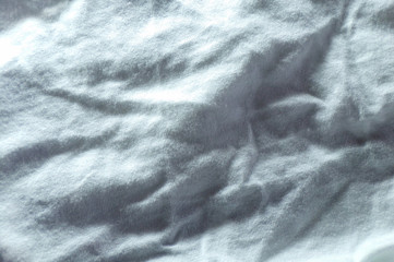 Crumpled fabric with white folds as an abstract textile background. Folds and waves on the white sheet.