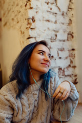 Fototapeta premium Young adult female with dyed blue hair listening music in a coffee shop during blue hour, shallow selective focus