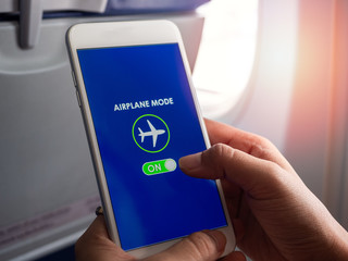 Flight mode concept. Hand holding white smartphone and turned on airplane mode on screen near the...