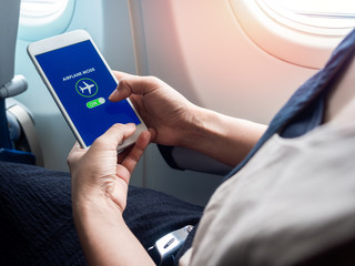 Flight mode concept. Hand holding white smartphone and turned on airplane mode on screen near the...