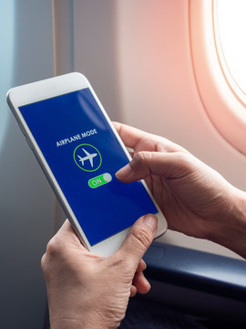 Flight mode concept. Hand holding white smartphone and turned on airplane mode on screen near the window on the airplane.