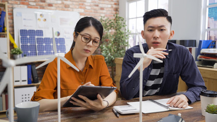 asian female and male colleagues coworking on model of manufacture with alternate supplies and energy saving systems. young woman and man architect discussing on windmill design wind power electronic