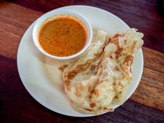 Breakfast Thai southern style. Roti with coconut milk curry in white dish on wooden table.