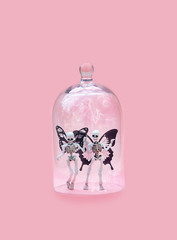 small skeletons under glass dome on pink background. surreal creative image. minimal concept.