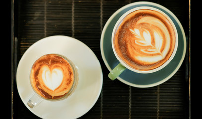 Coffee cups with heart and leaf art on dark tray, top view