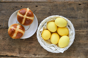 Easter cross buns with colored yellow eggs on a wooden background
