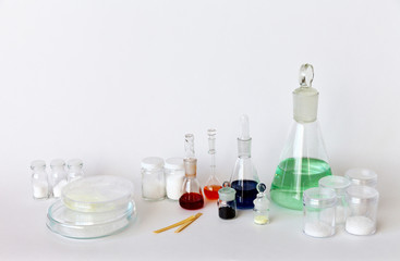 Chemical laboratory glassware with color solutions in flasks and reagents in jars and Petri dishes on a white background. The concept of chemical research. Copy space, close-up, blank, mock up