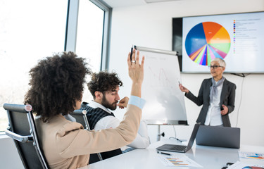 A manager showing a graph to other employees while one of the employees raised hand to ask a question.