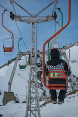 Backview of male tourist in winter clothes sitting on mountain chairlift. Travel destinations...