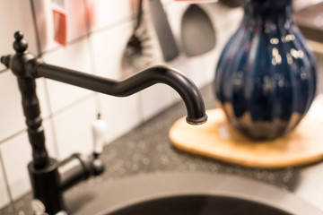 kitchen sink of dark gray stone with chrome faucet in a clean kitchen with a glossy work surface, close up faucet sink. Close up details of contemporary apartment kitchen.faucet and stainless sink