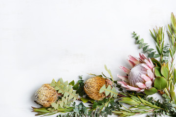 Beautiful floral arrangement of a pink King Protea and yellow/orange banksias surrounded by leucadendrons and Australian eucalyptus leaves creating a floral border on a white background.