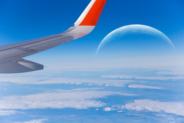 Naklejka na ściany i meble Wing of an airplane. Photo from the porthole of an airplane. Blue sky, white clouds, big moon. Aerospace flights.