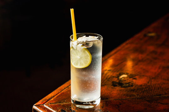 A transparent cocktail in a highball glass garnished with a lemon wheel, coconut chips and an eco straw made of macaroni