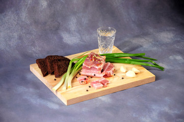 A wooden stand with a yummy vodka piece of lard with green onions, garlic and pepper is on a gray...