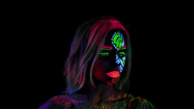 Close-up of Fashion Model with Flaming Colourful UV Pattern. Impressive Face of Authentic Style of Makeup. Ultra Violet paints on Female Face. Pink Hair, Glowing Shiny Eyes in Lenses. Trendy Body Art.