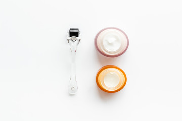 Dermaroller for mesotherapy near creams on white background top-down flat lay