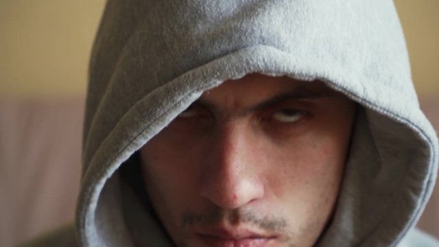 Beautiful Caucasian young guy with a beard in a gray hoodie and picks up an angry look. Portrait