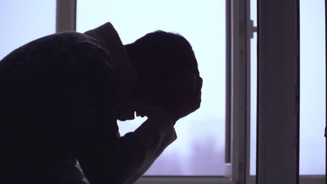 Silhouette. Guy sits and shouts holding his head. Depression and problems in life. Slow motion