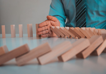 Businessman stopping domino effect with his hand, strategy and successful intervention concept for business.