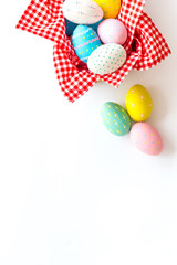 Easter eggs painted in basket on white desk top-down copy space