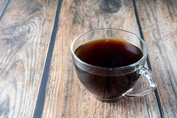 Coffee inside clear glass over wooden background.
