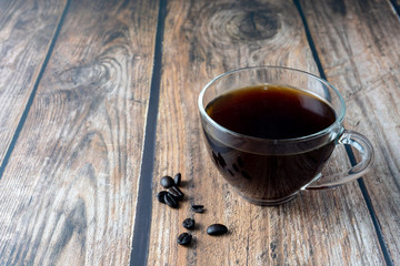 Coffee inside clear glass over wooden background.