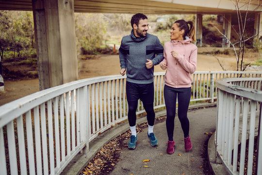 Full Length Of Dedicated Sporty Young Couple Ascending Bridge, Jogging And Looking At Each Other.