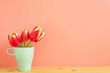 Red tulip flowers on wooden table with orange background. Spring floral arrangement, copy space