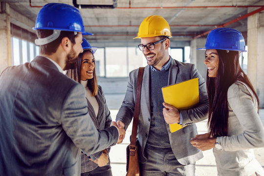 Smiling successful architect holding folder with contract in hands and shaking hands with businessman. Next to him are his female colleagues.