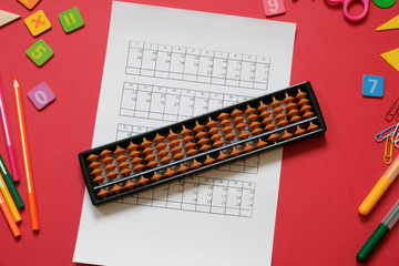 Mental arithmetic and Mathematics concept: colorful pens and pencils, numbers, abacus scores on red background