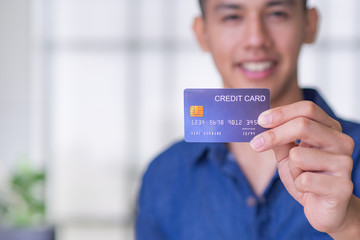 Young man wearing a blue shirt smiling and showing a blue credit card for prepare shopping online. Space for text. Concept of finance and e-commerce