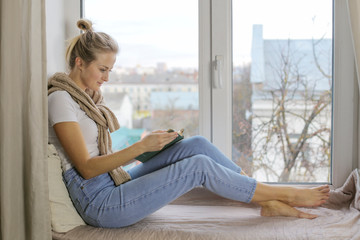 Young woman sitting on a windowsill and read interesting books