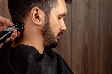 Obraz premium The master makes a haircut to the client with an electric machine, trimmer, close-up. The process of male haircuts at the hairdresser, barbershop. Body care, lifestyle, metrosexual.