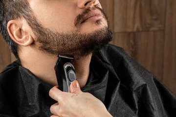 The master makes a beard haircut to the client with an electric machine, trimmer, close-up. The process of shaving a beard at the hairdresser. Body care, lifestyle, metrosexual.